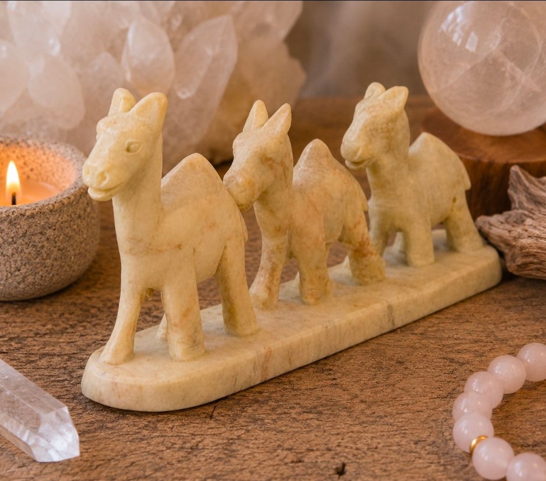 Drie kleine, kaarsvormige paardjes op een beige voetstuk, met kristallen en een brandende kaars op de achtergrond.