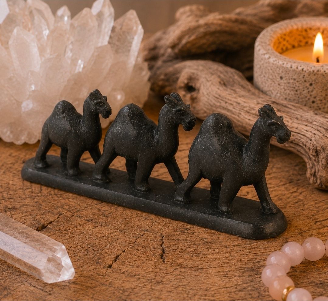 Zwarte kameelbeeldjes op een houten dienblad naast kristallen, een brandende kaars en kralenversiering.