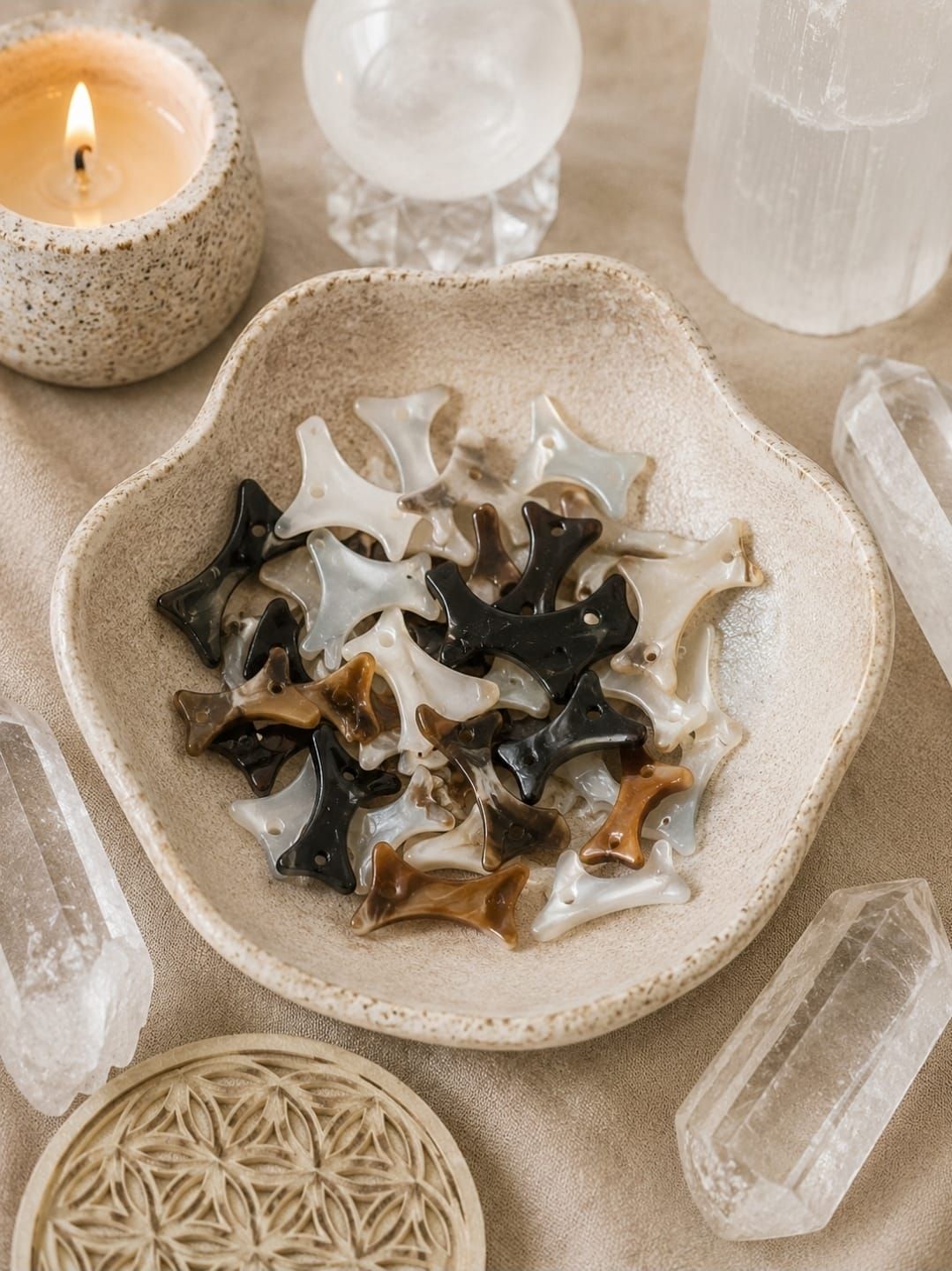 Diverse kristallen sterren en schelpen in een beige schaal naast kaarsen en transparante stenen.