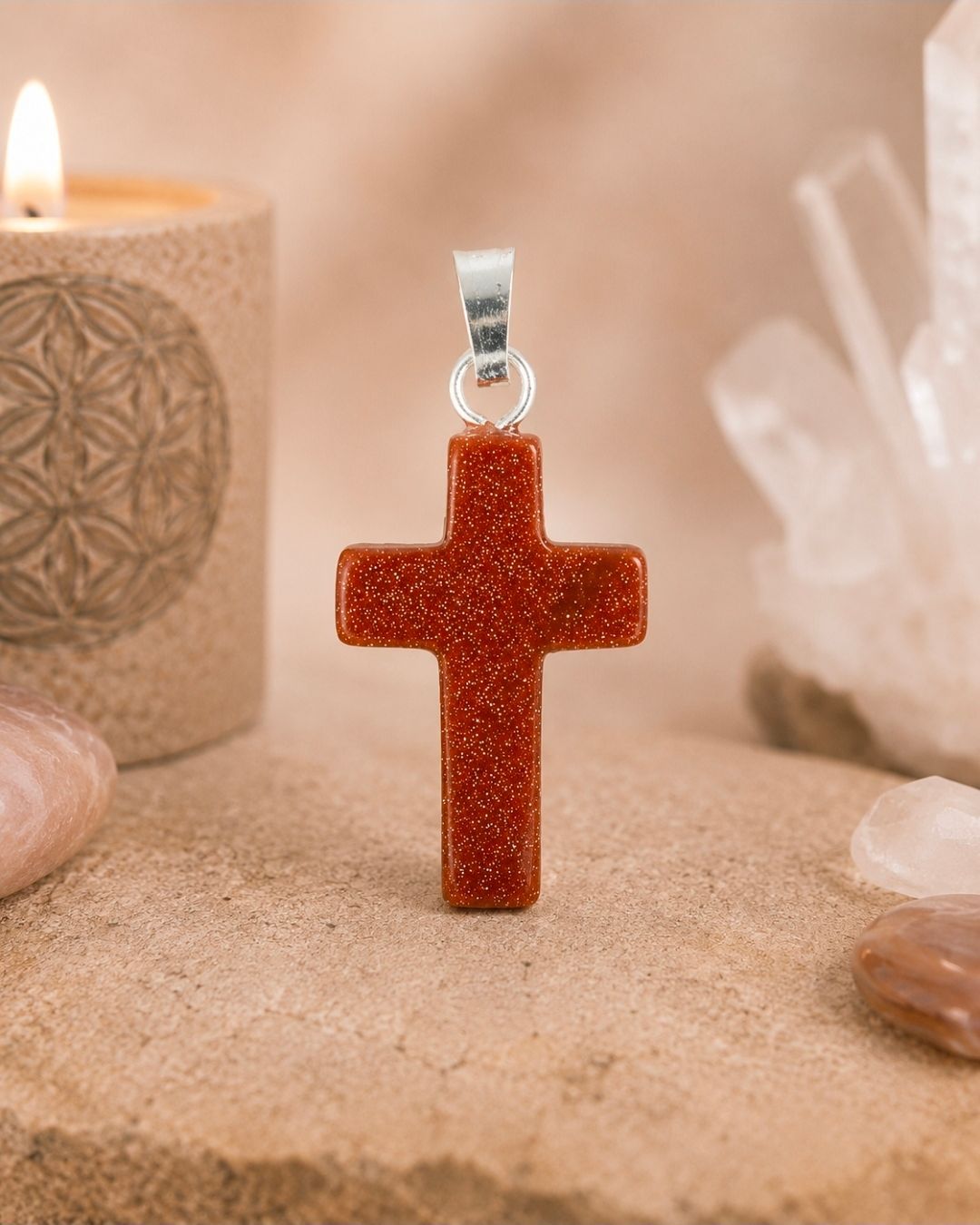 Oranje glitter kruishanger hangend tegen een zachtbeige achtergrond van kristallen en kaarsen.