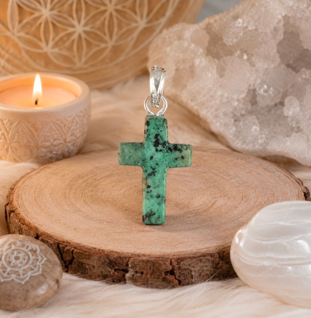 Groene stenen kruishanger aan een koord, tentoongesteld op een houten schijf met kaars en kristallen.