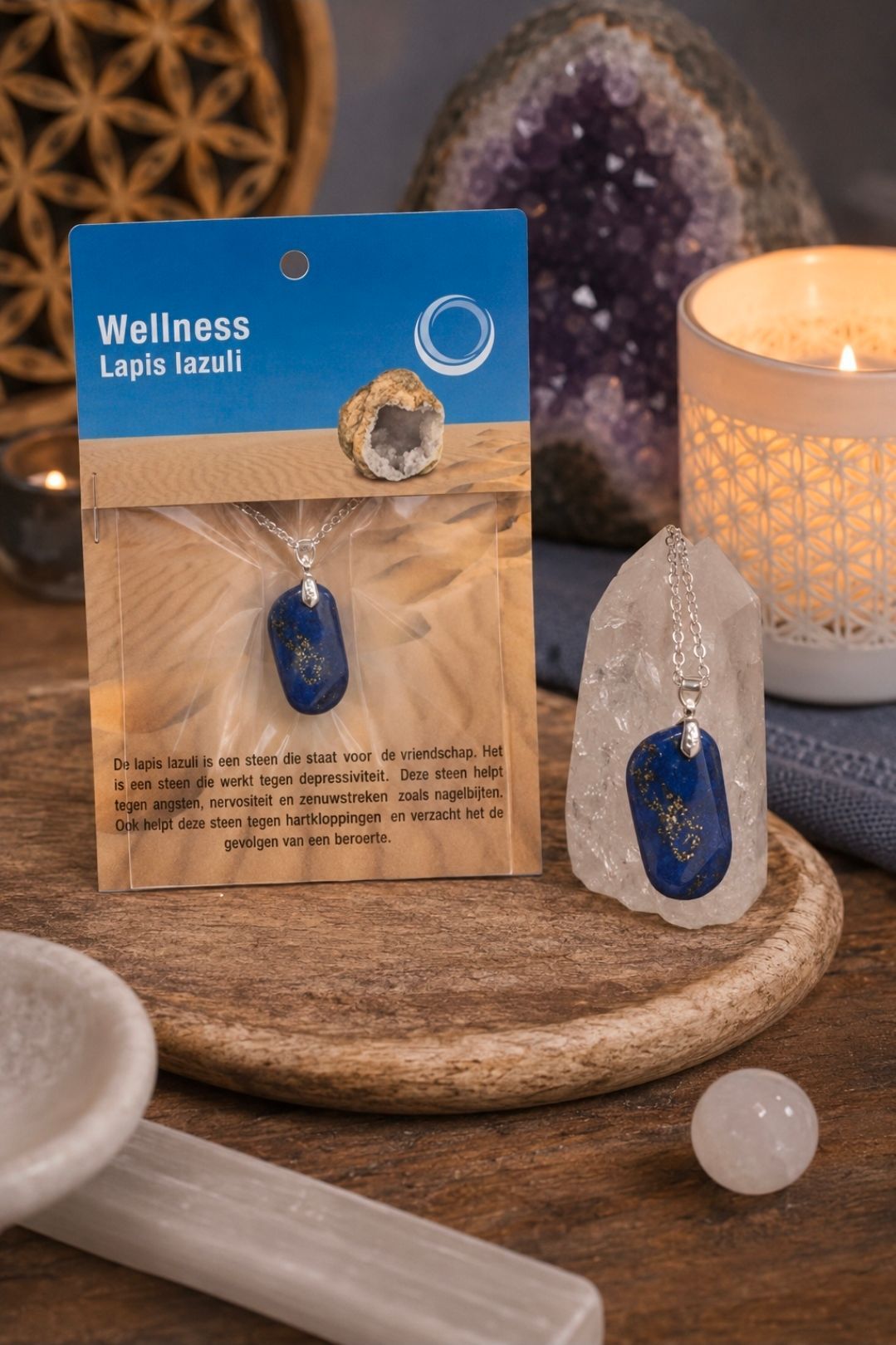 Een display met blauwe hangers, naast een brandende kaars, kristal en salie op een houten ondergrond.