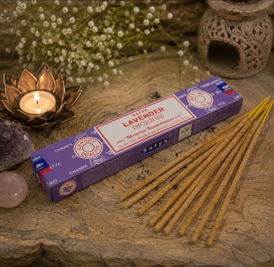 Lavendelwierookstokjes en een doosje op een rustieke ondergrond met een brandende kaars en bloemen.