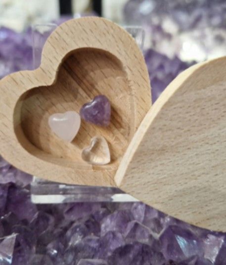Houten hartvormig doosje met kleine kristallen op een amethistkleurige achtergrond.