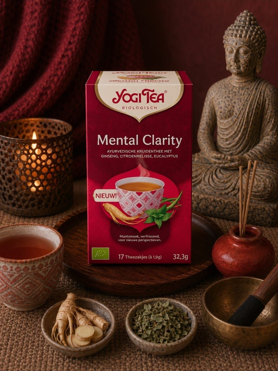 Yogi Tea Mental Clarity-box met thee-ingrediënten, kaars, kopje en Boeddhabeeldje op een tafel in warme tinten.