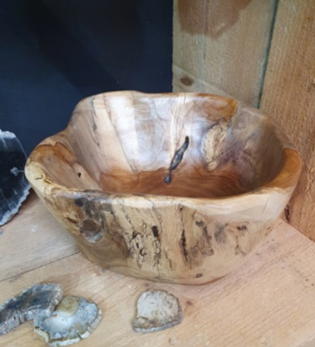 Een houten kom op een tafelblad, met kleine steentjes ervoor en een houten muur erachter.