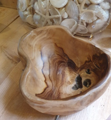 Een houten kom op een tafelblad, met kleine steentjes ervoor en een houten muur erachter.