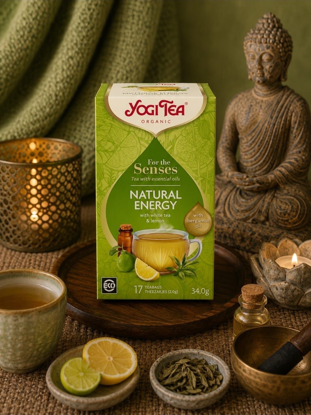 Een doos Yogi Tea Natural Energy met thee en limoen op een houten tafel, naast kaarsen en een Boeddhabeeld.
