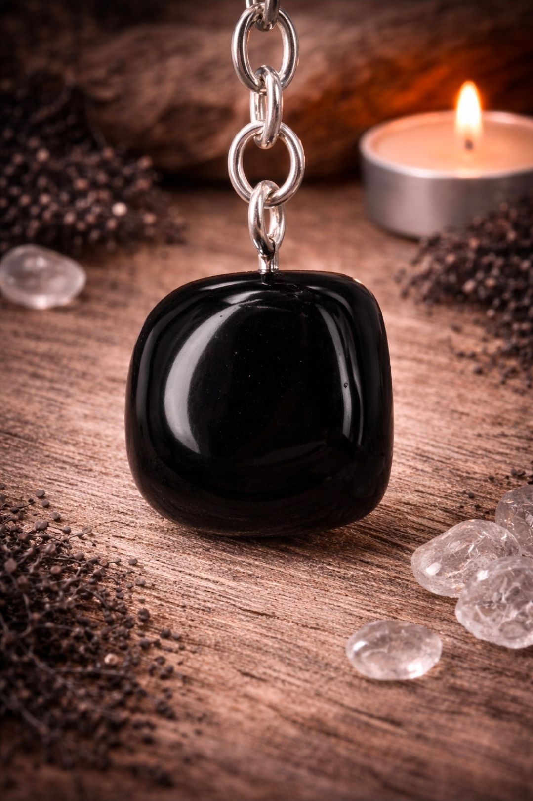 Zwarte hanger aan een zilveren ketting naast een brandende kaars en heldere kristallen op een houten ondergrond.