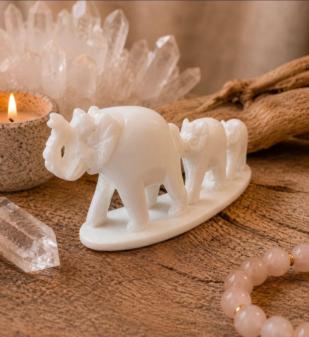 Een houtsnijwerk van een witte olifant op een houten ondergrond, naast een kaars en kristallen.