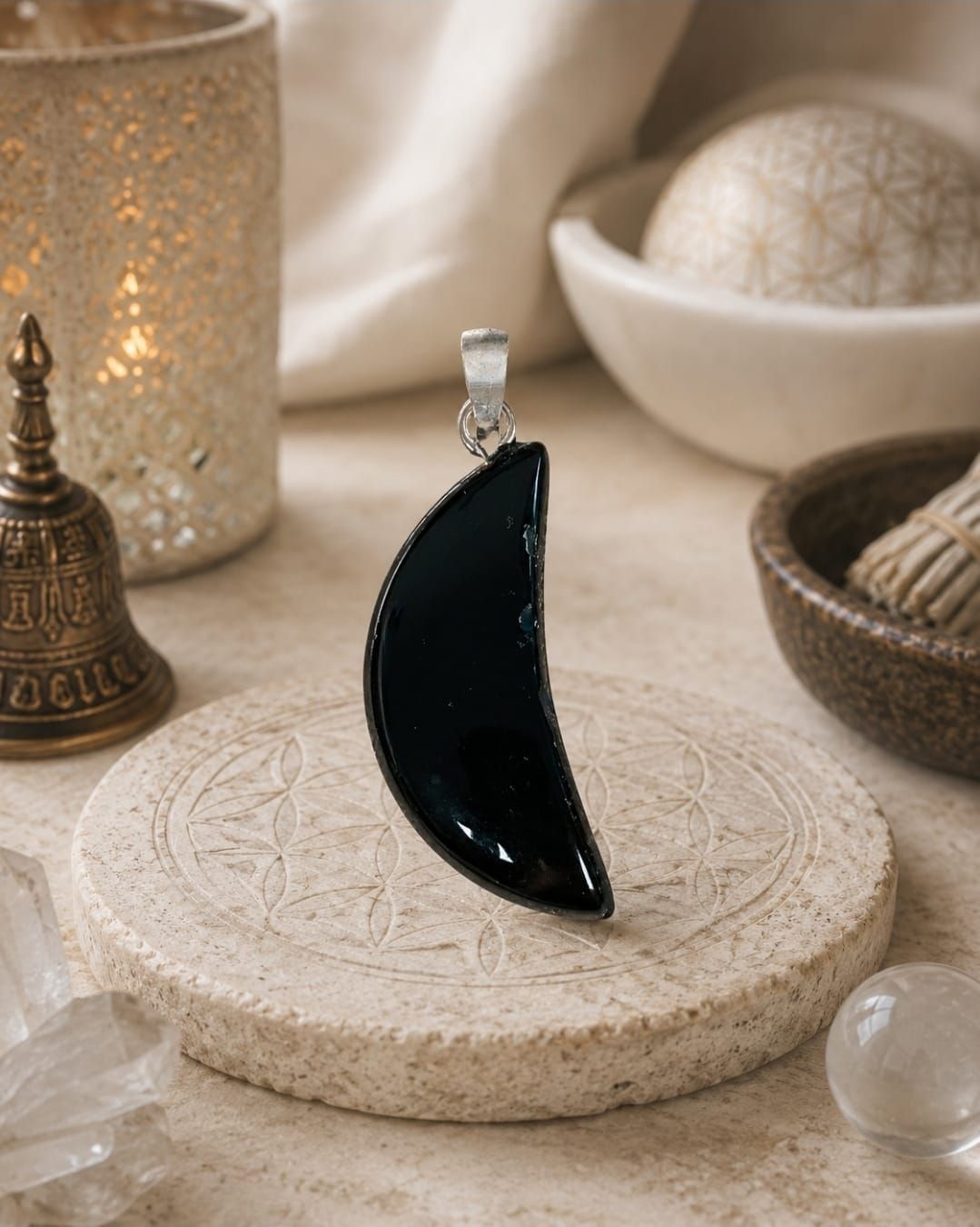Zwarte halvemaanvormige hanglamp op een beige, gestructureerde voet met warme decoratieve kaarsen en schalen