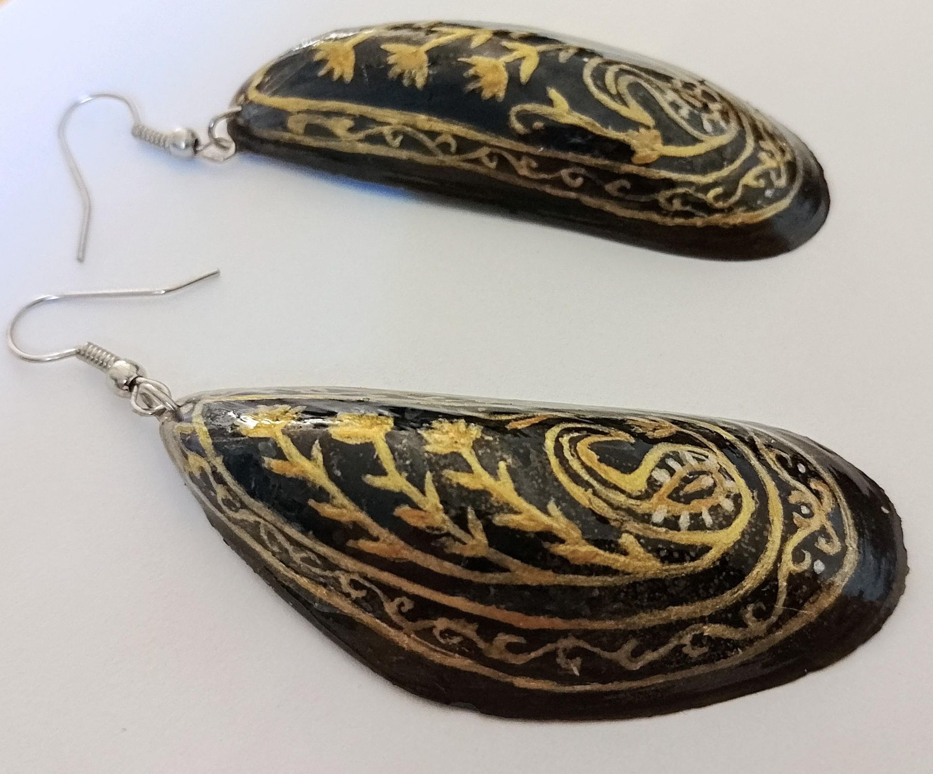 Een paar zwarte en gouden druppelvormige oorbellen met bloem- en spiraalpatronen op de haakjes.