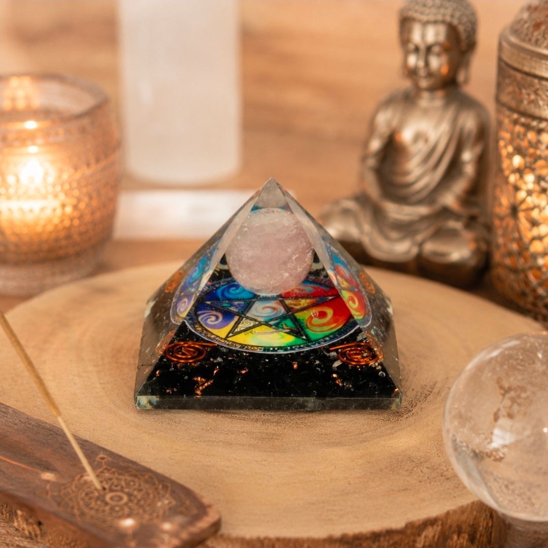 Kristallen piramide op een houten ondergrond met een kleurrijk chakra-ontwerp, kaarsen, een Boeddha-beeldje en een transparante bol.