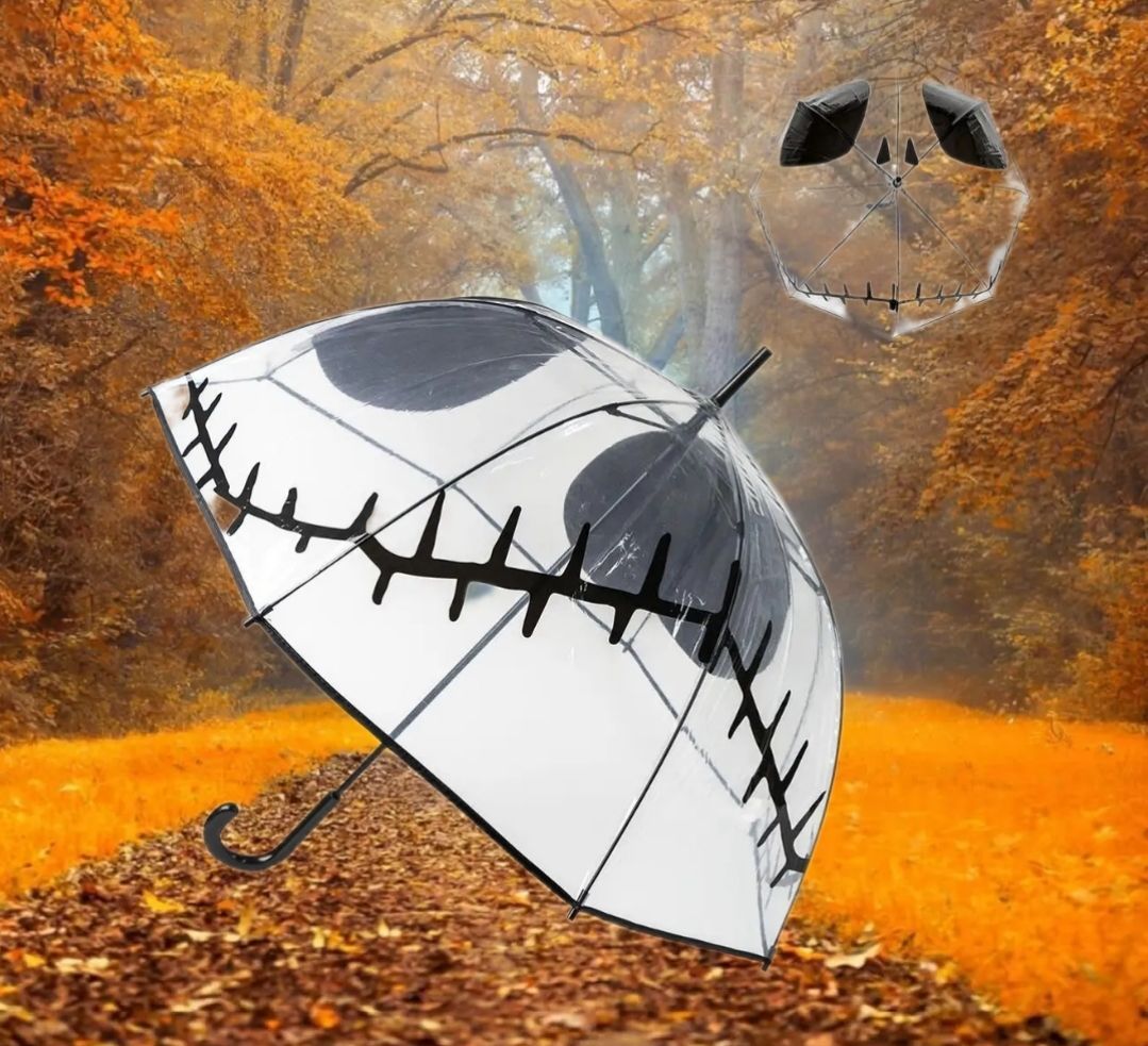 Witte paraplu met zwarte stiknaad in een oranje herfstbos, met een klein donker voorwerp erboven.