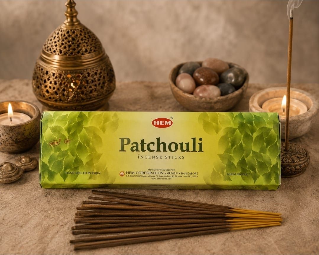 Een doosje met patchouli-wierook, brandende kaarsen, messing decoratie, een schaal met steentjes en wierookstokjes op een warme tafel.