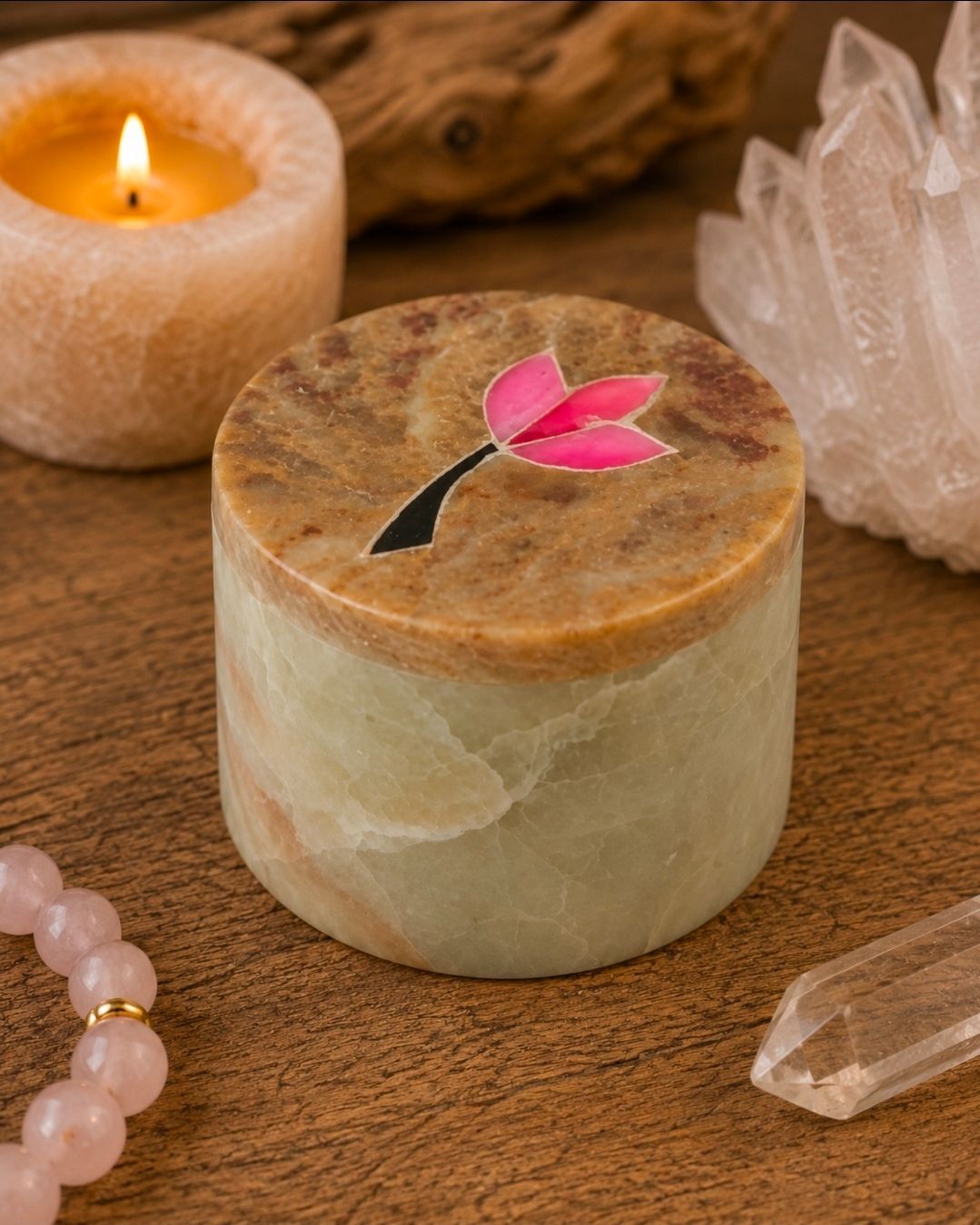 Ronde kaars met roze bloem, brandende kaars en kristallen op een houten ondergrond.