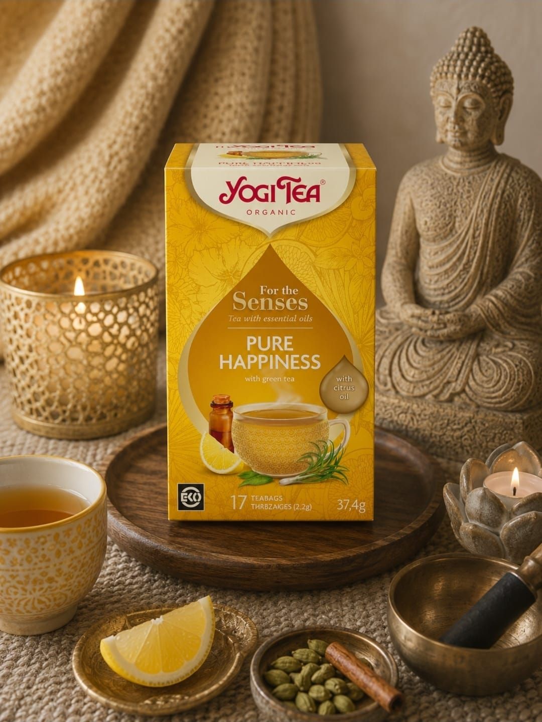 Yogi Tea Pure Happiness-doos met theeaccessoires, kaarsen en een Boeddhabeeldje op een warme beige achtergrond.