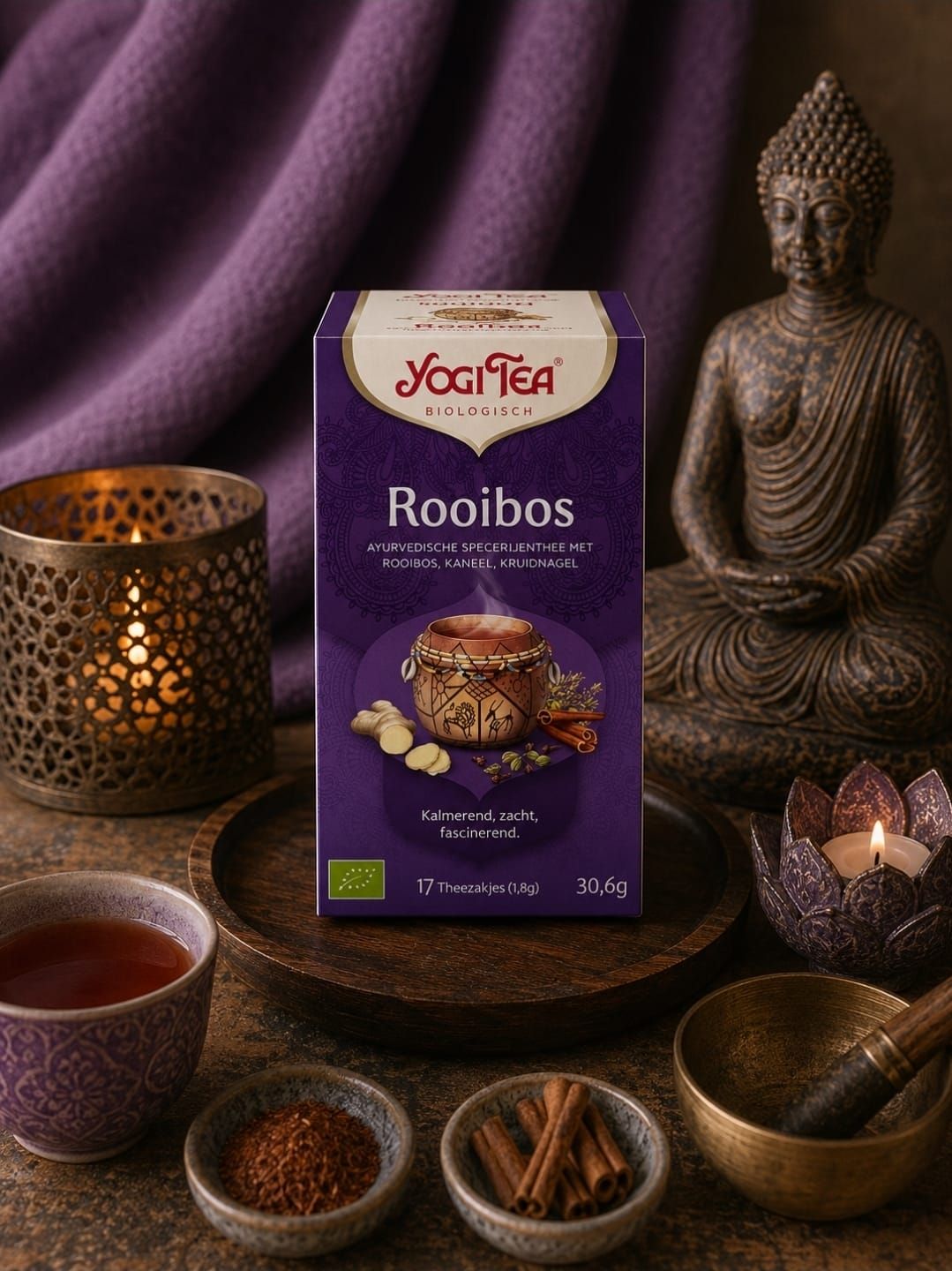 Yogi Tea Rooibos-doos met theekopjes, kaneelstokjes en een Boeddhabeeldje op een paarse achtergrond.