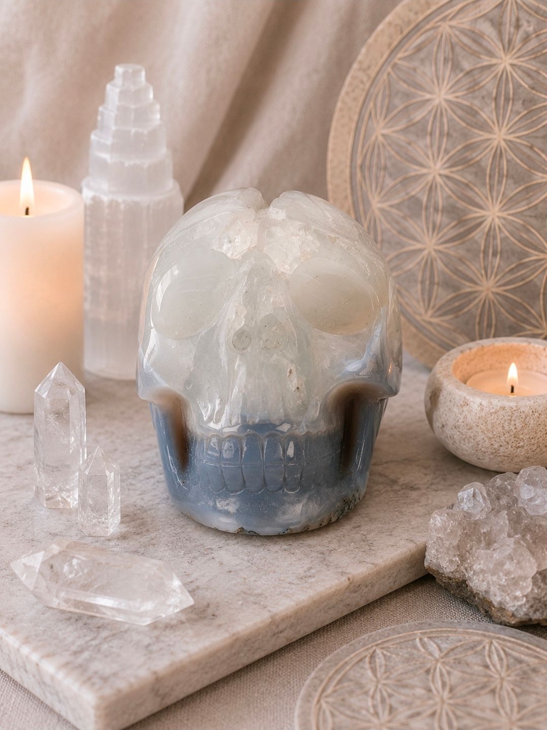Kristallen decoratie en brandende kaarsen op een stenen dienblad, met een witte geode als middelpunt en seleniettorens.