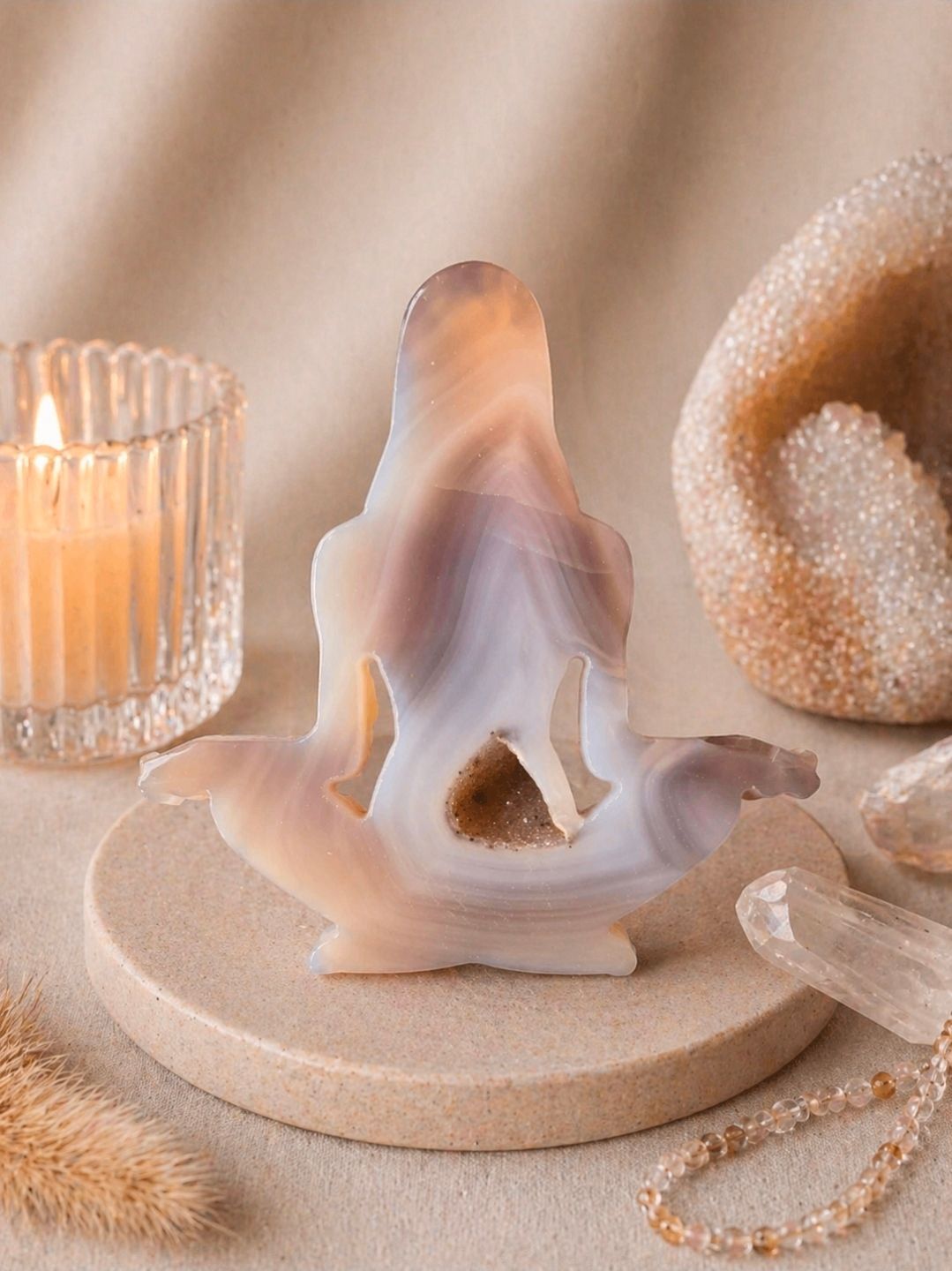 Zachte, wit-beige, sculpturale decoratie op een ronde sokkel met kaarsen, een geweven ring en parelsnoeren.