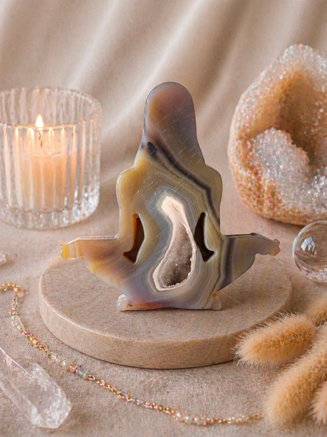 Kristallen geode in kandelaarvorm op een houten dienblad met warm kaarslicht en zachte beige decoratie.