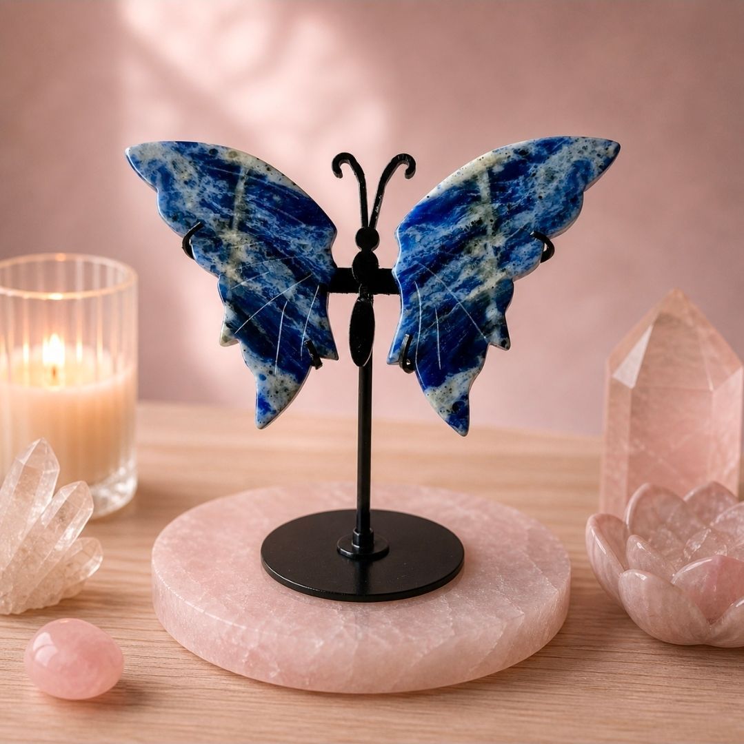 Een blauw vlinderbeeldje op een voetstuk, tentoongesteld op een roze stenen schijf met kristallen versiering en een kaars.