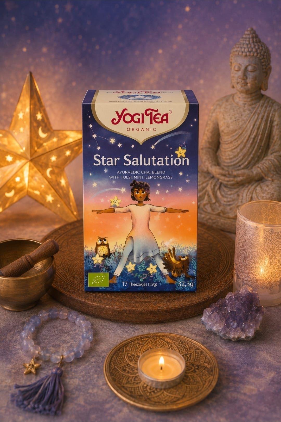 Een doosje met de Yogi Tea Star Salutation op een altaar bij kaarslicht, met een Boeddhabeeld, kristallen