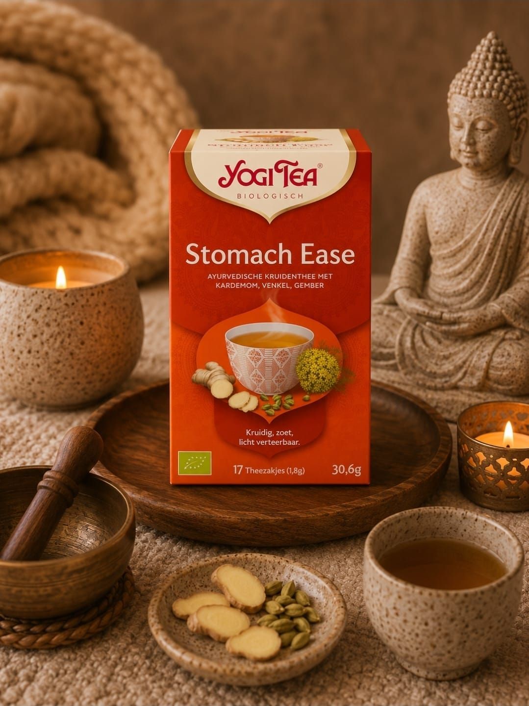 Een doosje Stomach Ease-thee tussen kaarsen, theekopjes, plakjes gember en een Boeddhabeeld in een warme spa-omgeving.