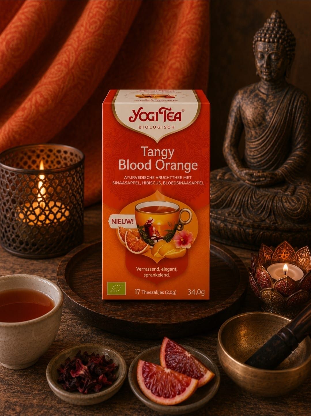 Een doos Yogi Tea Tangerine Blood Orange met theekopjes, sinaasappelschijfjes, kaarsen en een Boeddhabeeldje