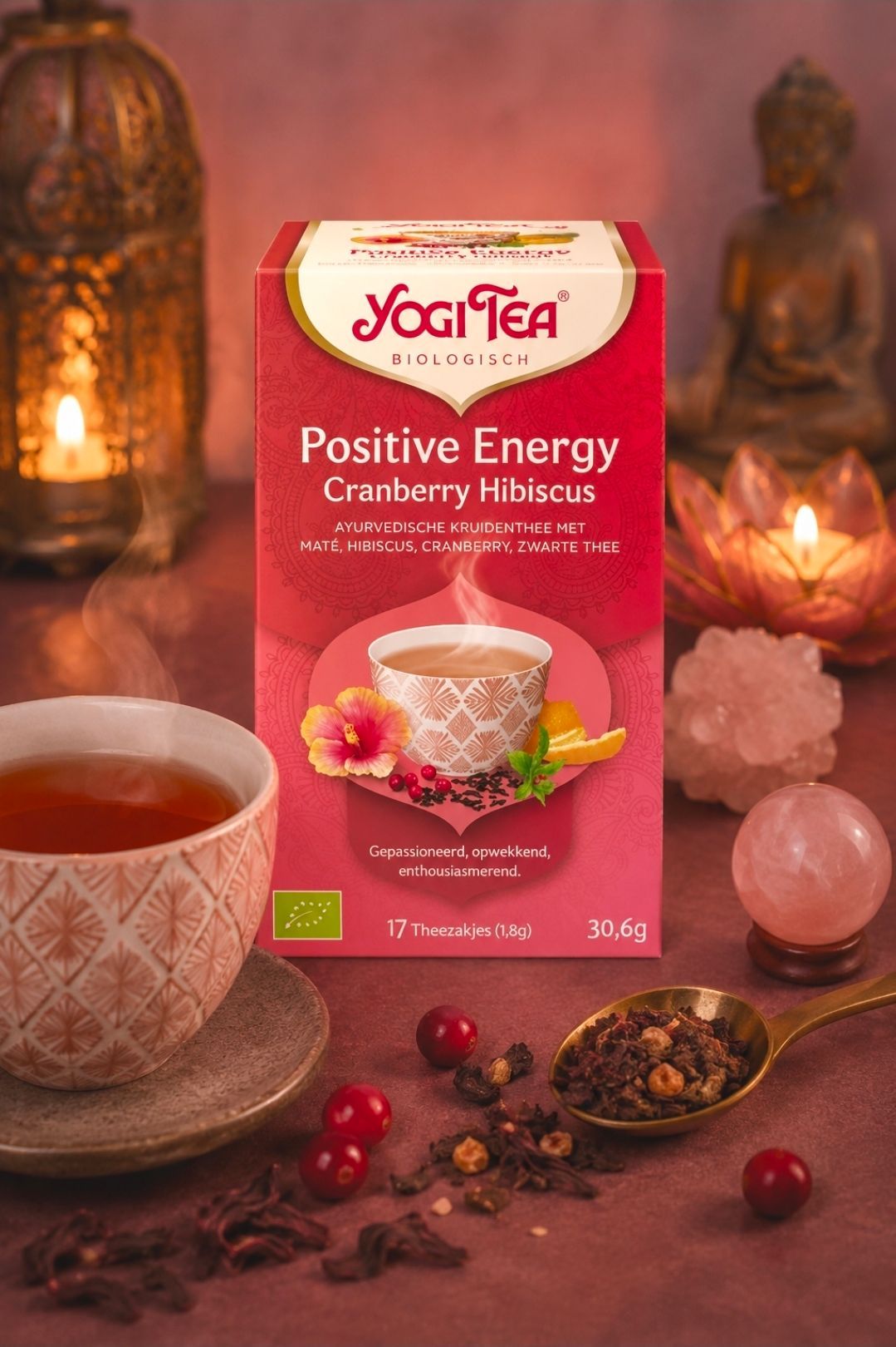Yogi Tea Positive Energy Cranberry Hibiscus theedoos met kopje, cranberries en kaarsen op een warm tafelblad.