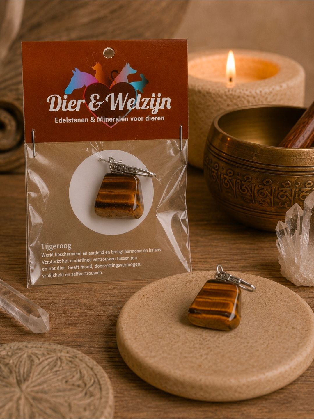 Een hanger van tijgeroog op een presentatiekaartje naast een brandende kaars en een bronzen schaal op een beige ondergrond.