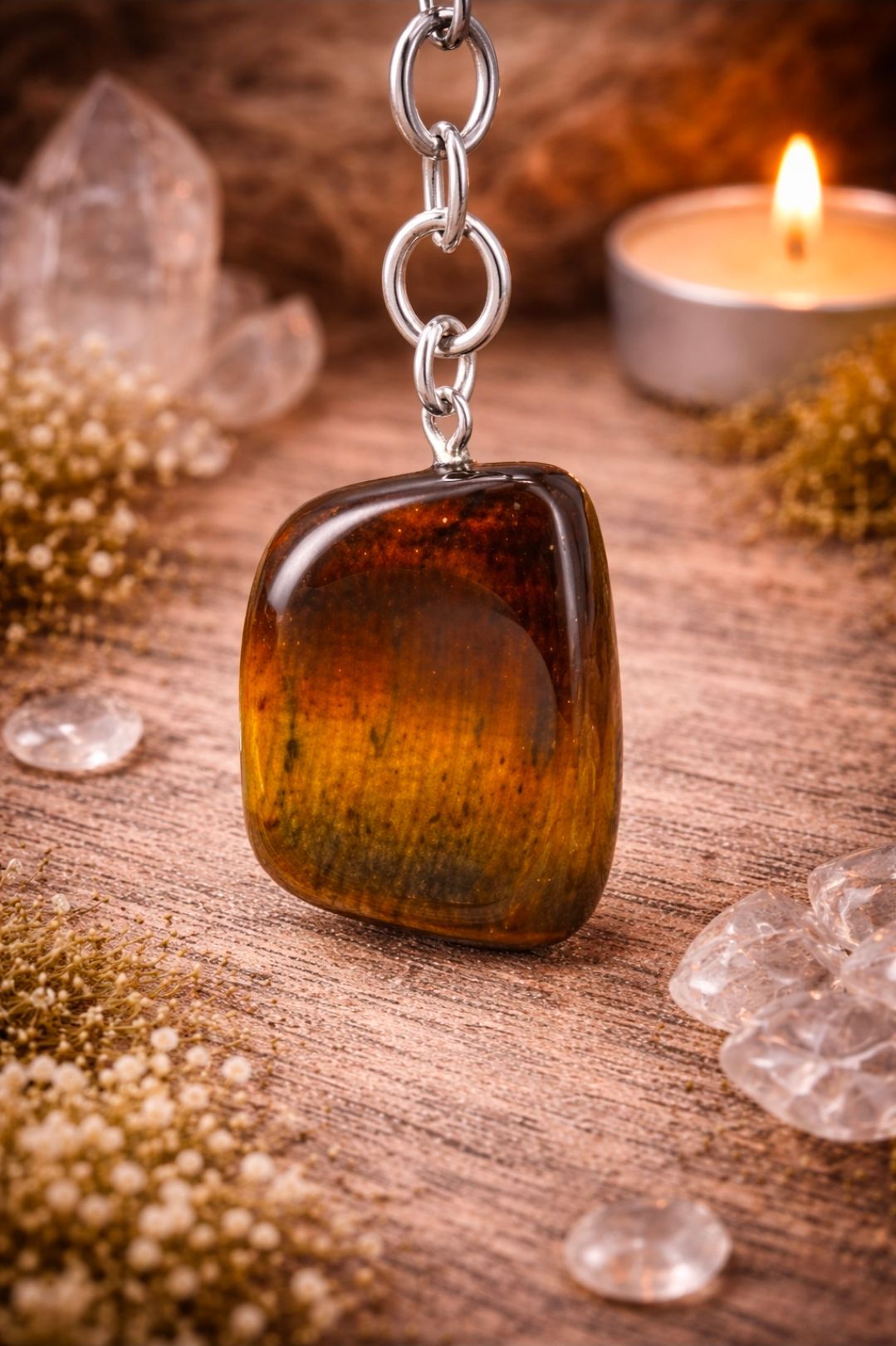 Een barnstenen hanger aan een ketting op een houten ondergrond, met kristallen en een brandende kaars op de achtergrond.