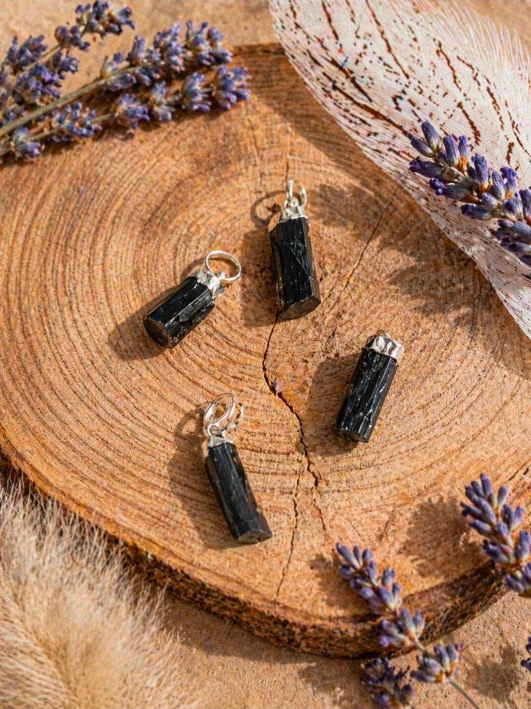 Vier zwarte kristallen hangers, geplaatst op een houten ondergrond met lavendeltakjes eromheen.
