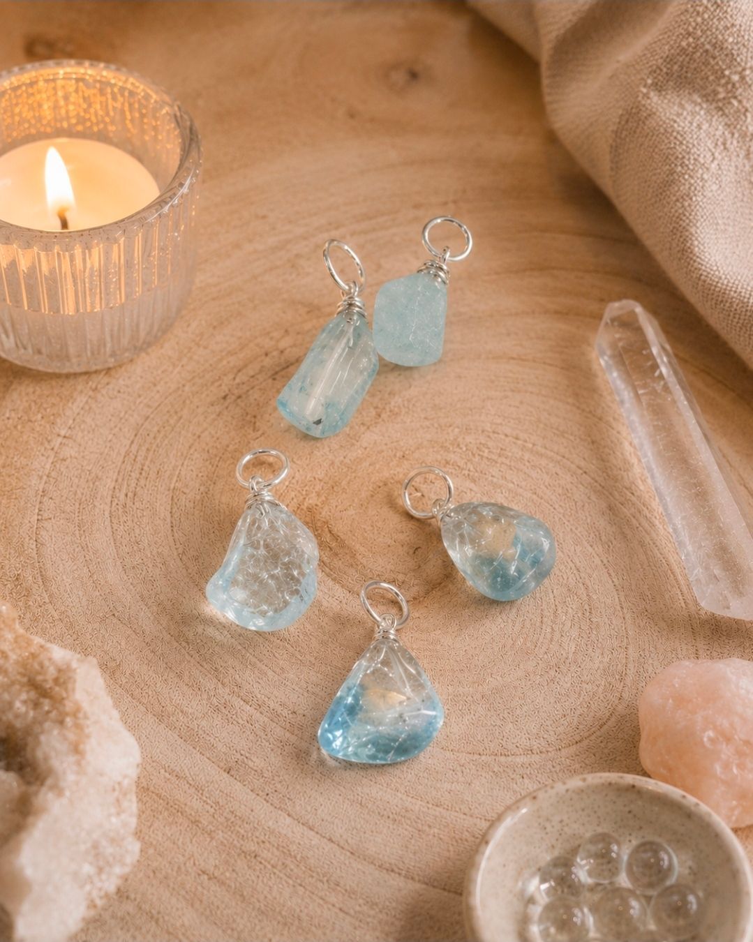 Kettingen met blauwe kristallen hangers op beige stof naast een brandende kaars.