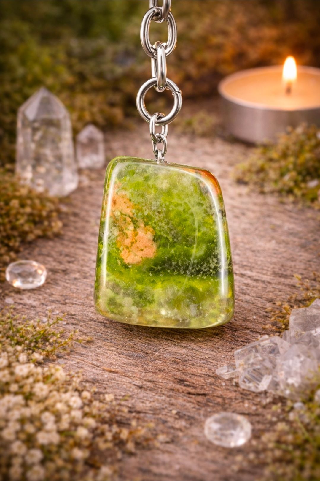 Groene, mosachtige hanger aan een ketting op een rustieke ondergrond met kristallen en een brandende kaars.