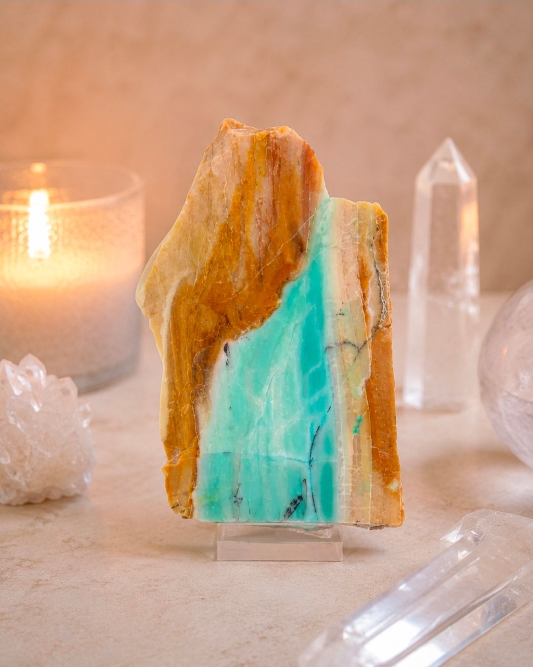 Een sculptuur van turquoise en beige kristallen op een tafel, met een kaars en transparante kristallen op de achtergrond.