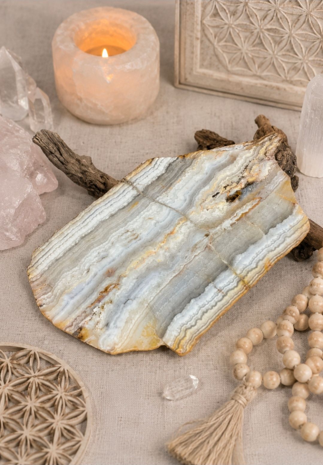 Decoratieve kristallen schijf op een beige ondergrond met een brandende kaars, houten kralen en geweven accenten.