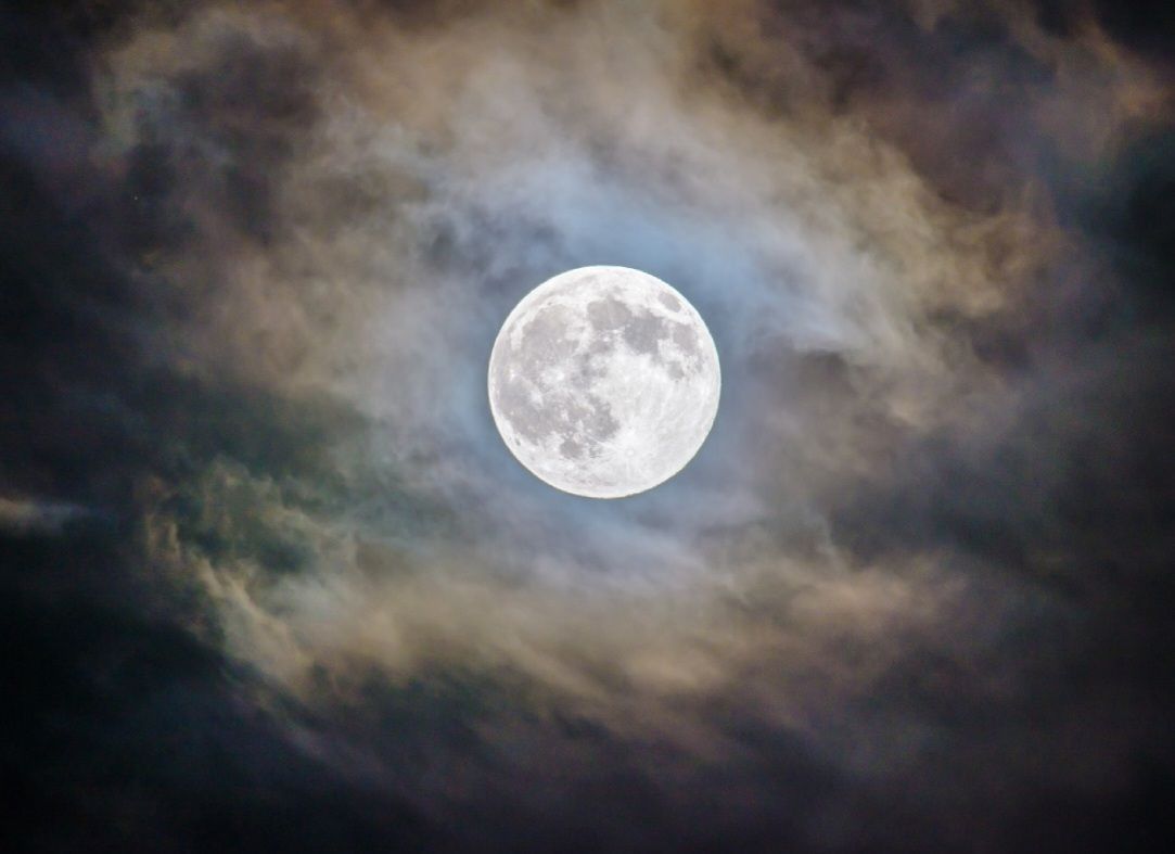 Volle maan die door donkere, wervelende wolken aan de nachtelijke hemel schijnt.