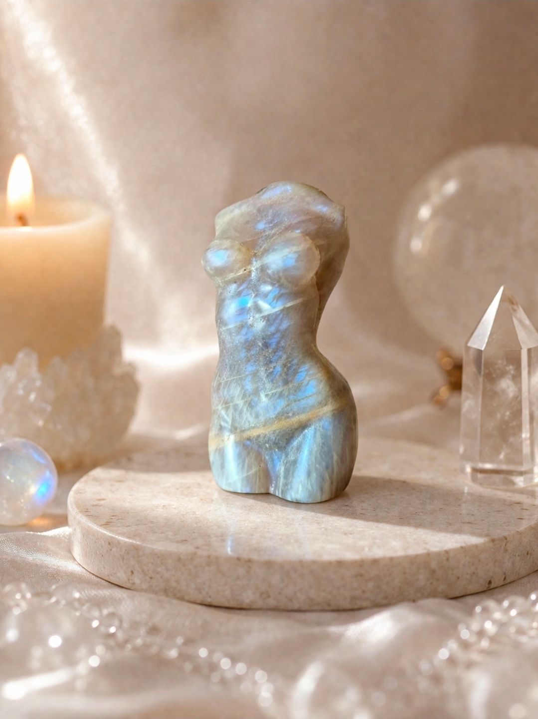 Blauw iriserend kristallen beeldje op een ronde sokkel naast een brandende kaars en heldere kwartspunten.