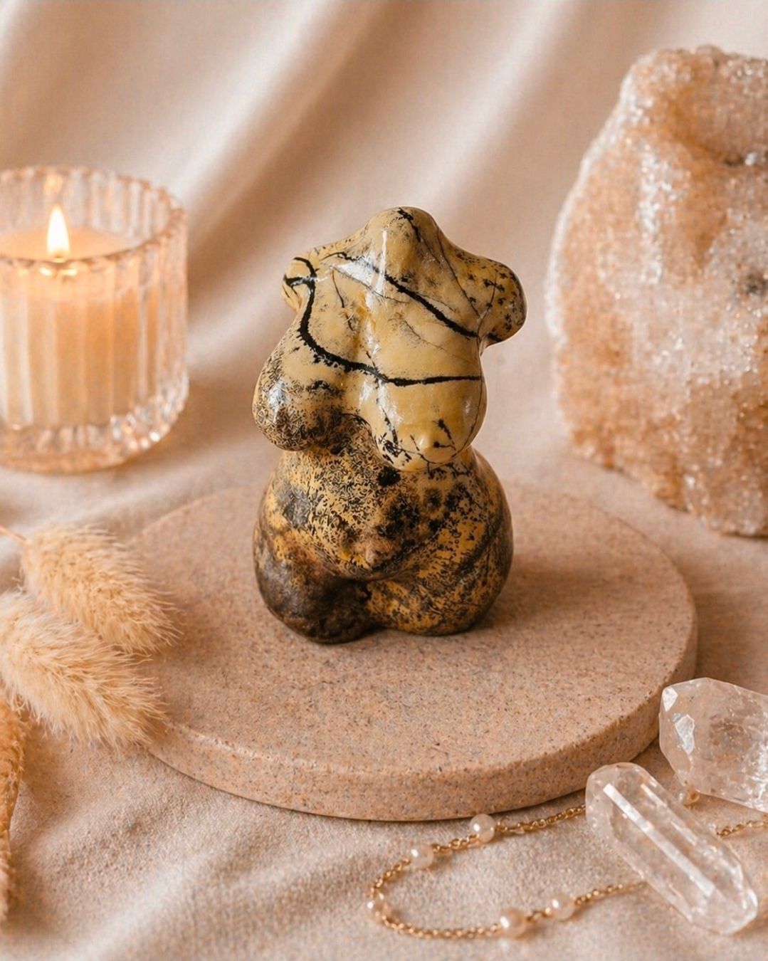 Klein, gemarmerd teddybeerbeeldje op een beige sokkel met kristallen versiering en een brandende kaars.