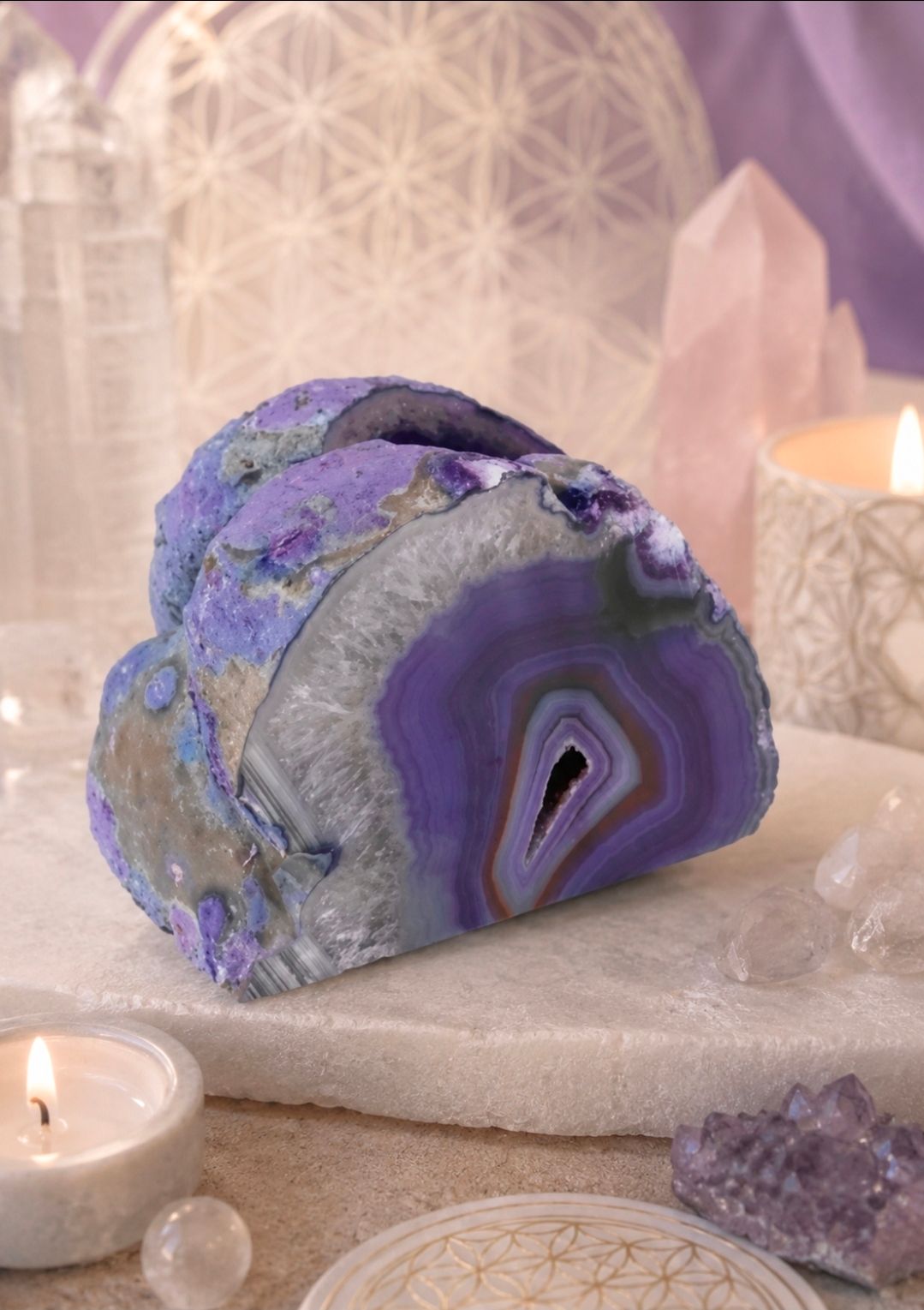 Paarse en grijze gepolijste kristallen geode op een display bij kaarslicht, omringd door kristallen en decoratieve stenen.