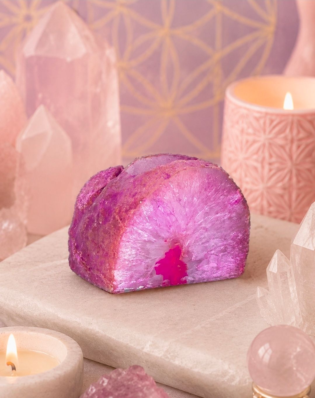 Roze kristallen geode op een beige plaat met kaarsen en rozenkwartsstenen