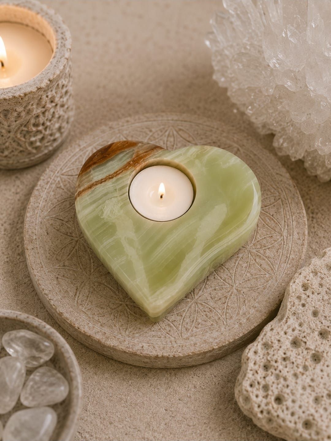 Groene hartvormige kaarsenhouder met een brandend theelichtje op een beige, gestructureerd oppervlak, omringd door stenen en kristallen.