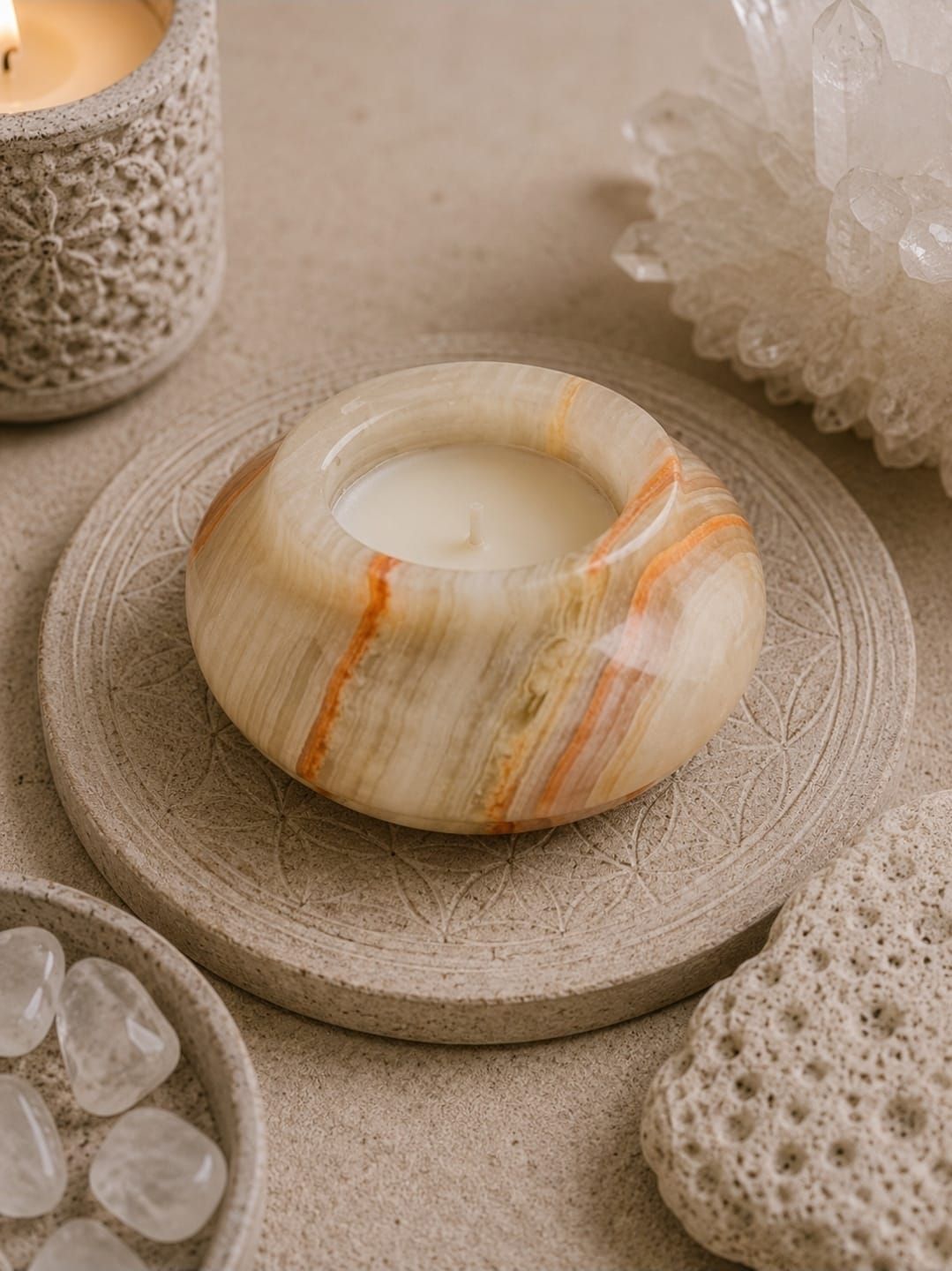 Crèmekleurige stenen kaars op een geweven onderzetter met zeeglas en decoratieve elementen in een beige omgeving.