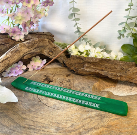 Groene wierookhouder met een brandend wierookstokje op een rustieke houten ondergrond, omringd door bloemen en groen.