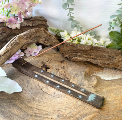 Decoratieve wierookhouder met sterreninleg op drijfhout, omringd door bloemen en groen.