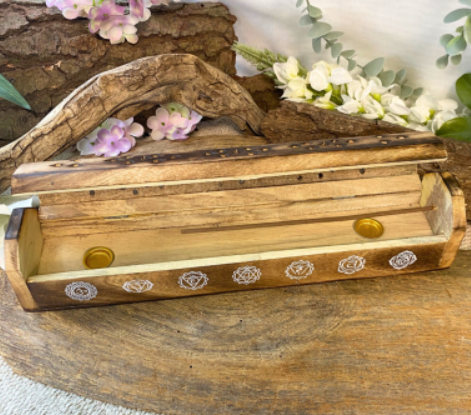 Houten bewaardoos met witte bloemenversiering, rustend op een rustieke houten ondergrond met bloemen erachter.