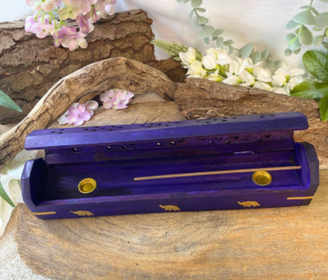 Paarse houten sieradendoos met gouden accenten op een rustiek houten oppervlak, versierd met bloemen.