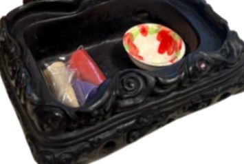Klein zwart draakje op een gebeeldhouwde sokkel, zittend op een houten ondergrond met een wazige, bladerrijke achtergrond.