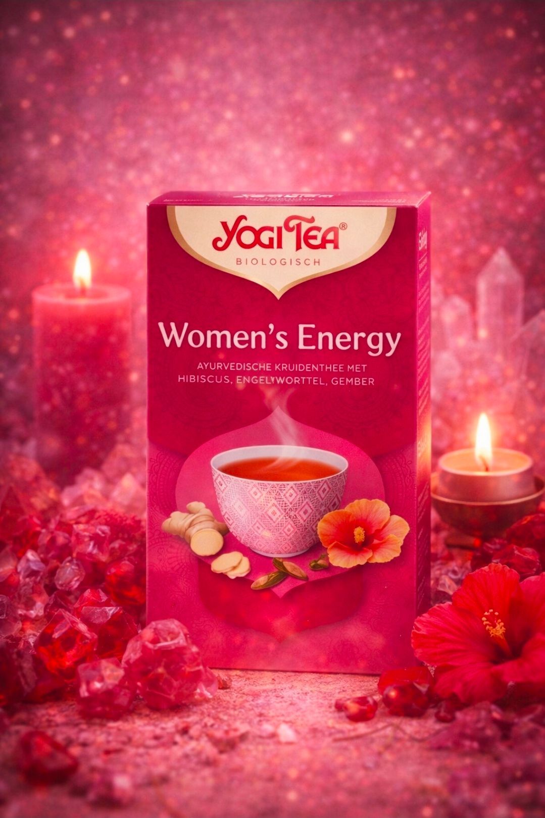 Roze Yogi Tea Women's Energy-box met een roze theekopje, bloemen en gloeiende kaarsen op een sprankelende roze achtergrond.